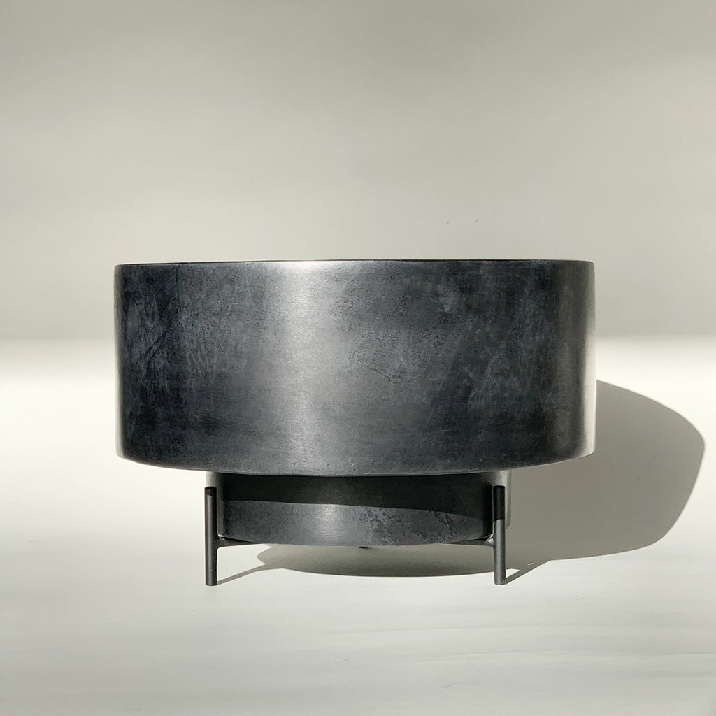 Image of M+A NYC Low Cylindrical Planter that is 8 1/8" in diameter, made of black soapstone with a low luster waxed finish, on a black powder coated brass stand.