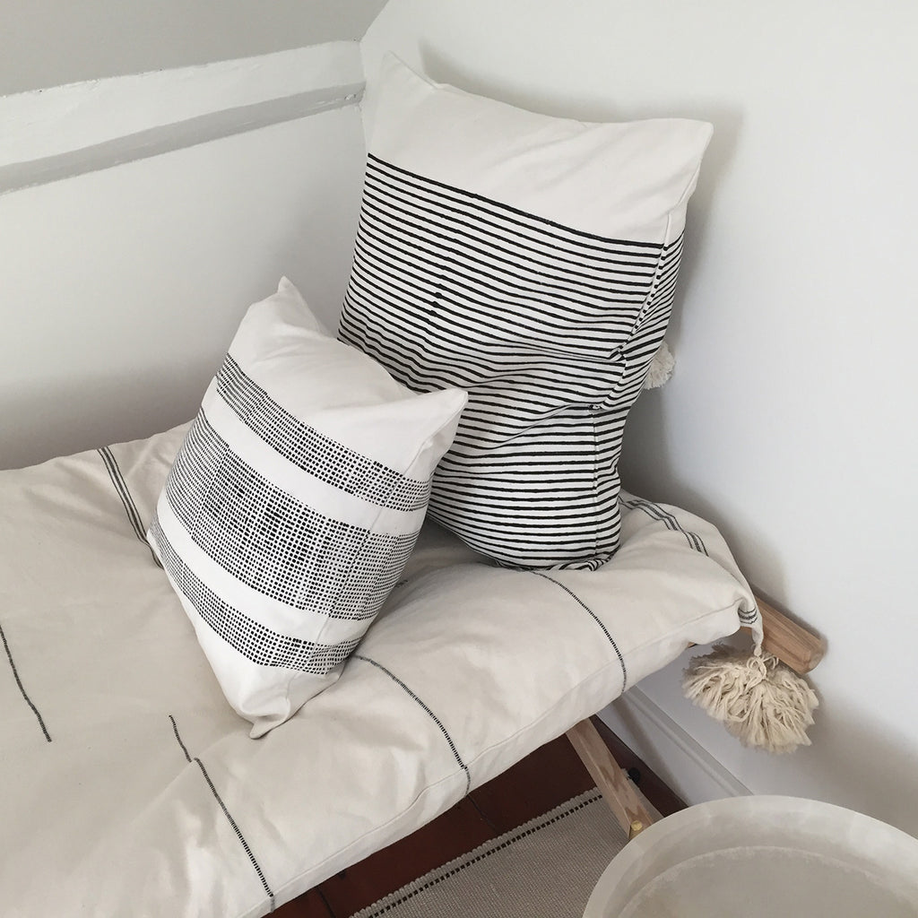 Image of M+A NYC's Block Print Pillow in the Breton Stripes  24" Square resting on a cot and paired with a smaller block print pillow.