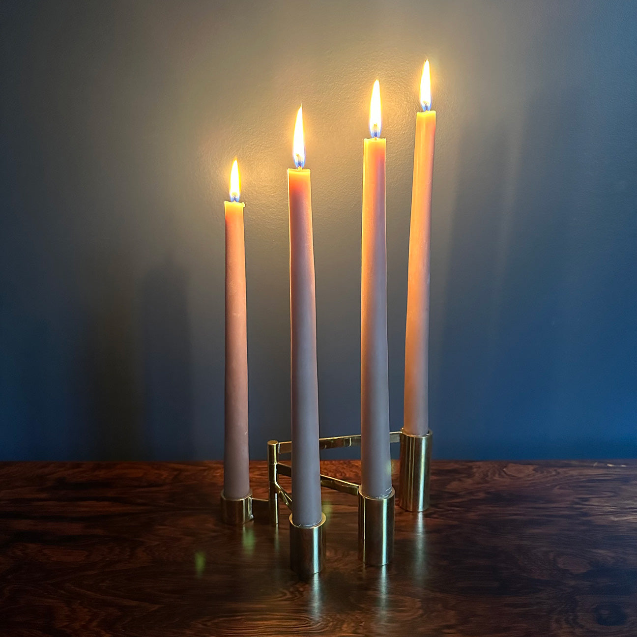 Image of M+A NYC Solid Brass Modular Swing Arm Candelabra with lit candles in the color "greige" sitting on a rosewood table against a blue green backdrop.