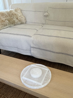 Image of M+A NYC Alabaster Trays, the Square sitting inside of the Round, both resting on a low table.
