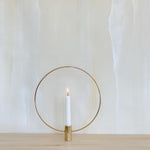Image of Halo Brass Taper Holder with lit white candle against Fromental wallpaper in the pattern Travertine