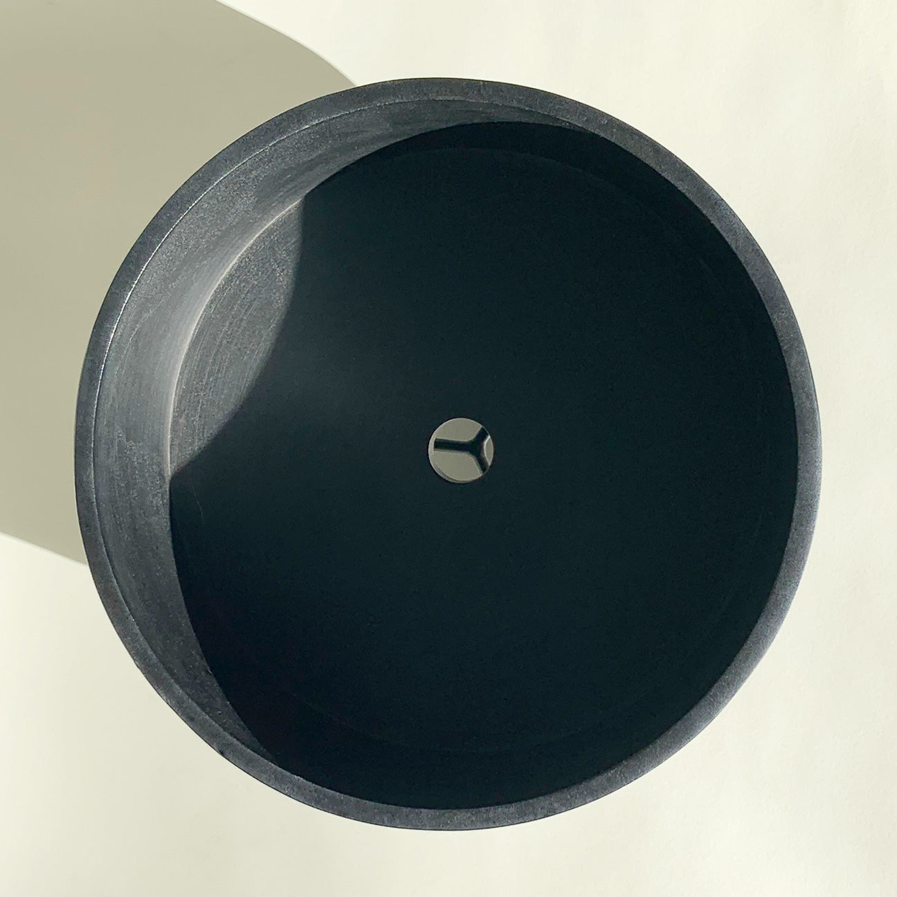 Top view of M+A NYC Low Cylindrical Planter that is 8 1/8" in diameter, made of black soapstone with a low luster waxed finish, on a black powder coated brass stand.