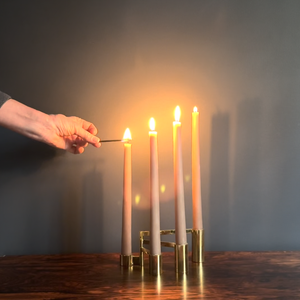 Image of candles being lit that are sitting in M+A NYC's Modular Brass Swing Arm Candelabra, atop a rosewood table and against a blue green backdrop.