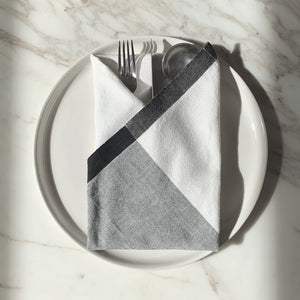 Image of M+A NYC Colorblock Napkin in Kora/Mineral folded on a cream plate with a set of flatware placed on top.