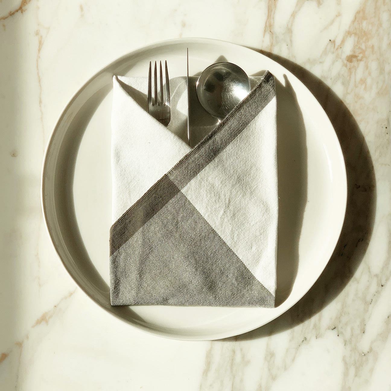 Image of M+A NYC Colorblock Napkin in Kora/Earth folded on a plate with cutlery nestled inside.