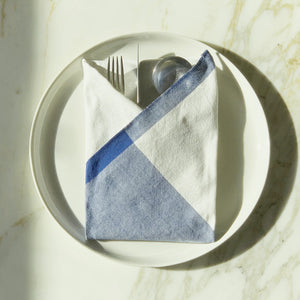 Image of M+A NYC Colorblock Napkin in Kora/Perfect Day folded on a cream plate with a set of flatware tucked inside.