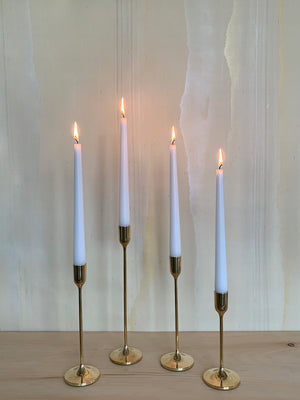 Image of 4 Solid Brass Taper Stands (1 Tall, 2 Medium, 1 Small) with lit candles on a wooden mantel against pale iridescent silk wallpaper by Fromental.
