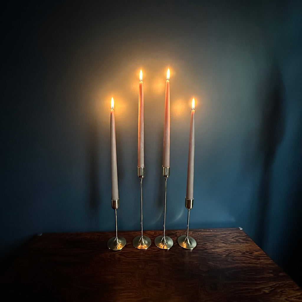 Image of 4 M+A NYC Solid Brass Taper Stands (2 Tall and 2 Small) with lit candles sitting atop a rosewood table against a blue green backdrop.
