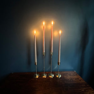 Image of 4 M+A NYC Solid Brass Taper Stands (2 Tall and 2 Small) with lit candles sitting atop a rosewood table against a blue green backdrop.